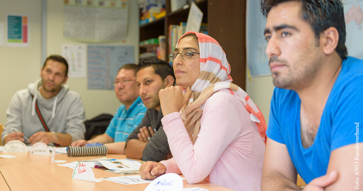 Vier Männer und eine Frau mit Kopftuch sitzen in einem Klassenzimmer und hören zu