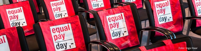 Symbolbild: Auf den Rückenlehnen von aufgereihten Stühlen ist das Logo des Equal Pay Day zu sehen. (Foto: Inga Haar)